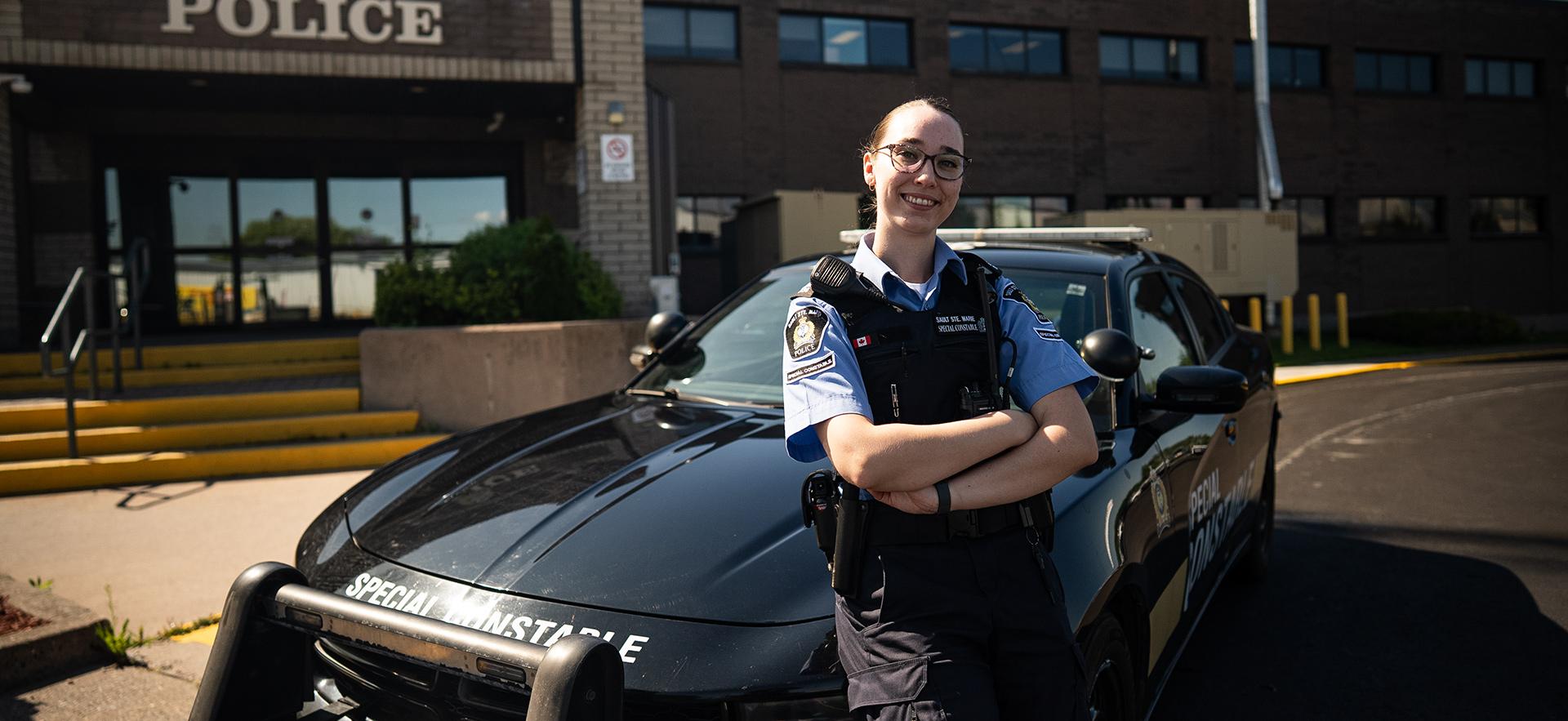 Policing graduate standing in front of cruiser at station