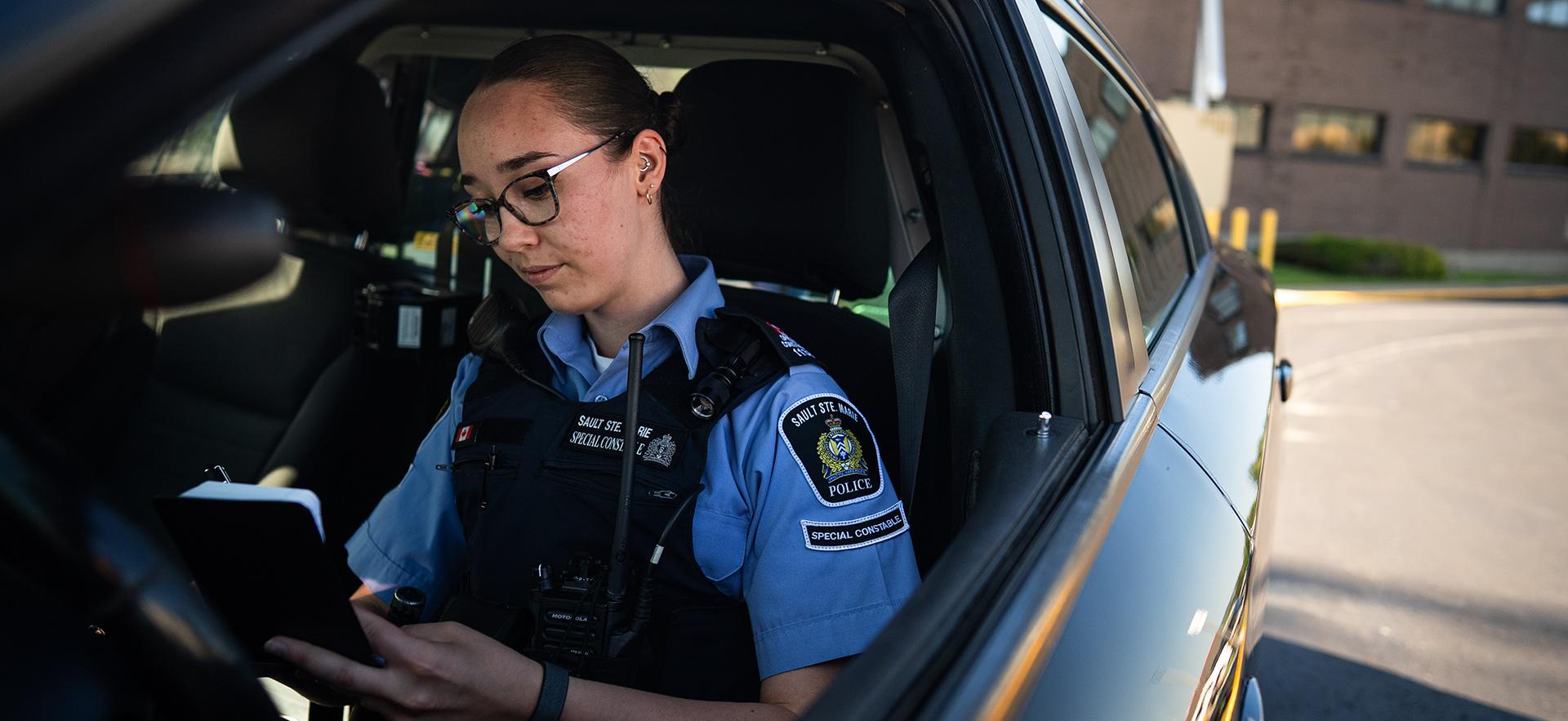 Policing grad as Constable in cruiser writing notes