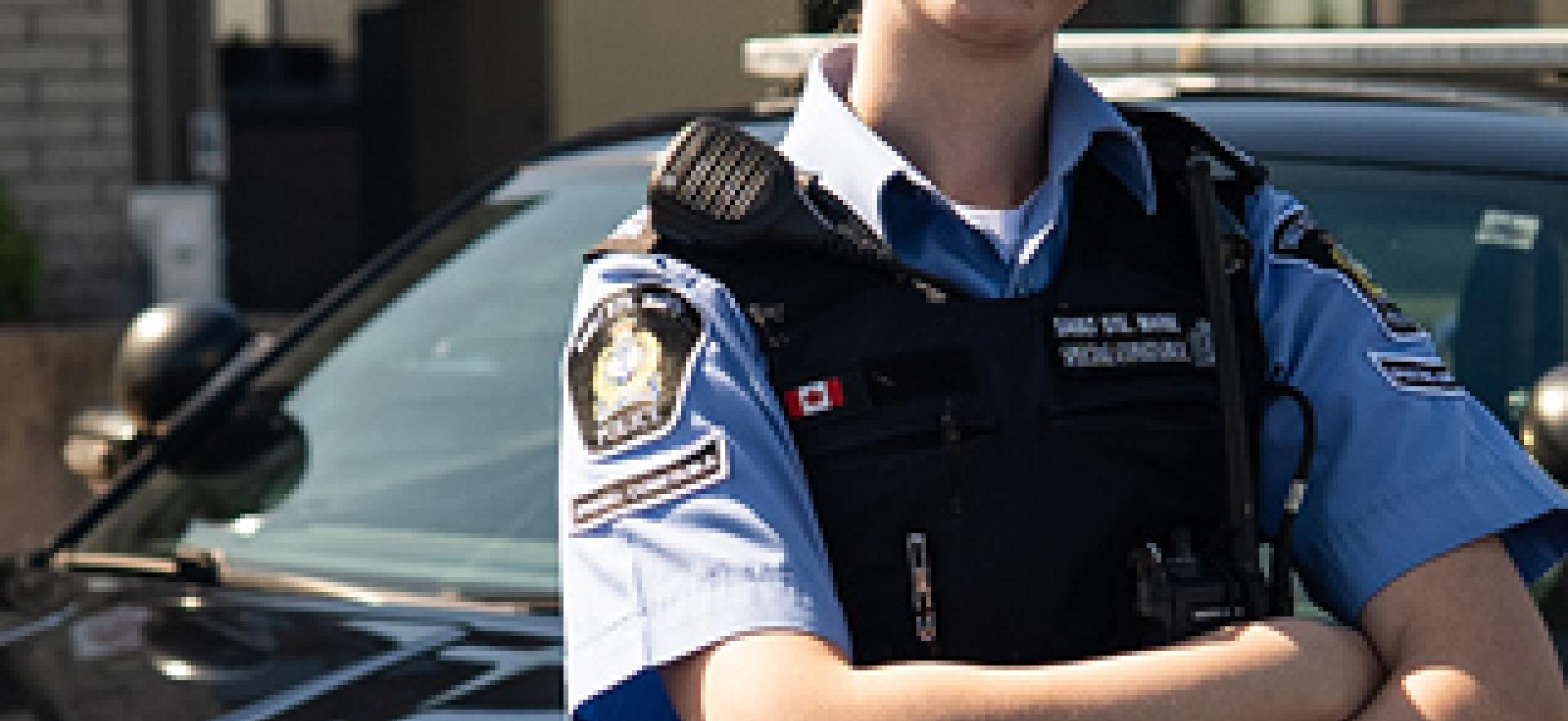 Policing graduate standing in front of cruiser at station