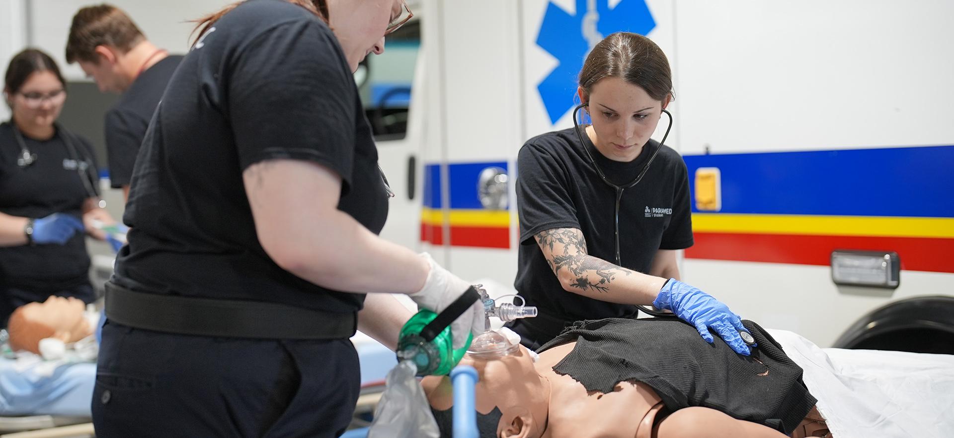 Paramedic students practicing skills in lab with manikin on stretcher