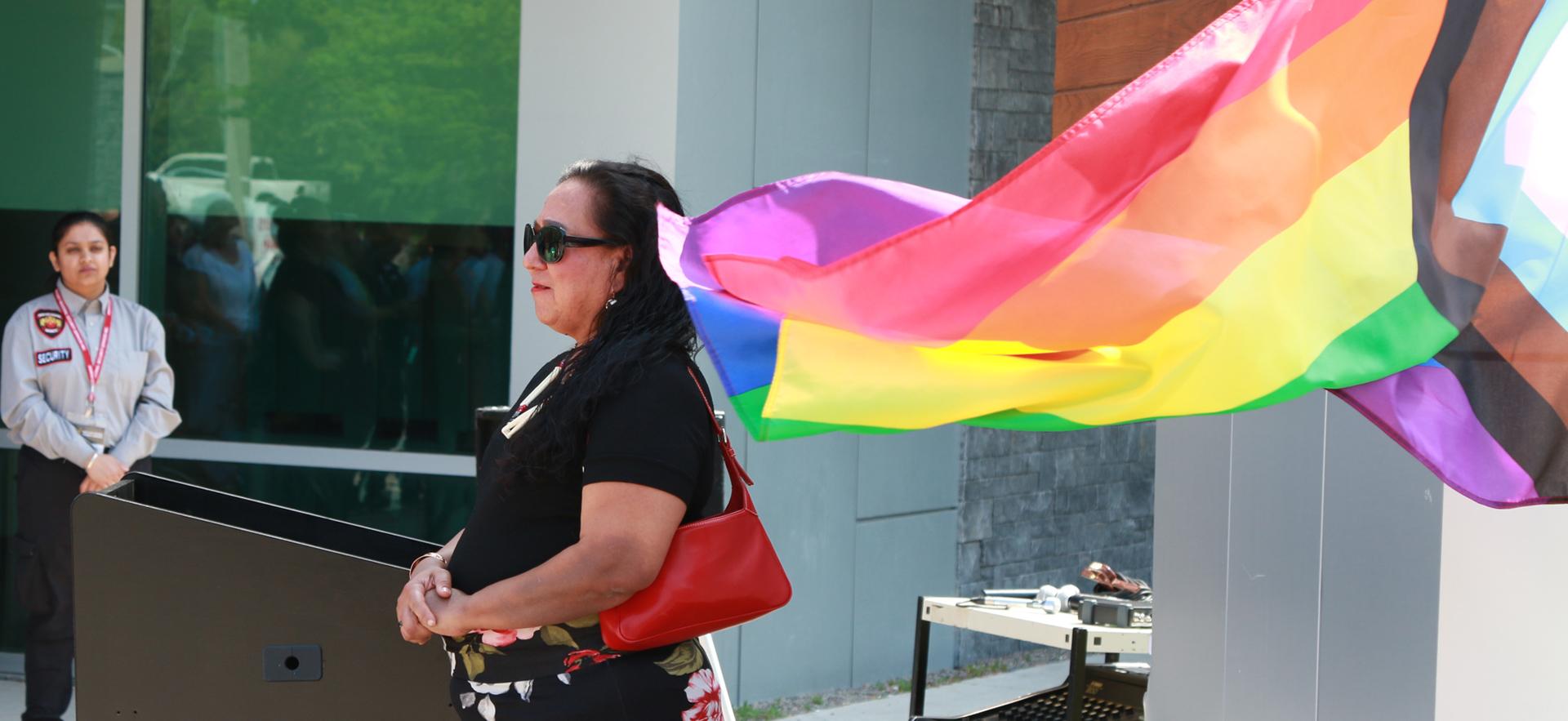 Pride flag being raised on flag pole with people in background