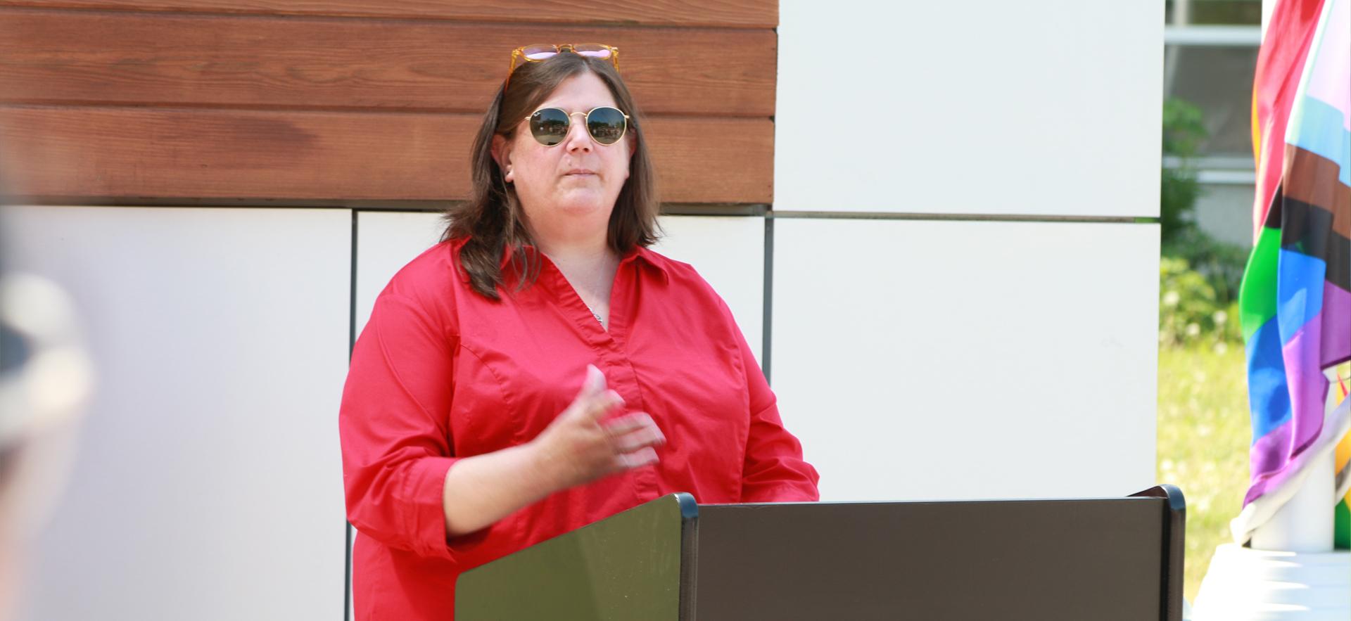 Kristen Auer at the podium speaking at the Pride Flag raising ceremony