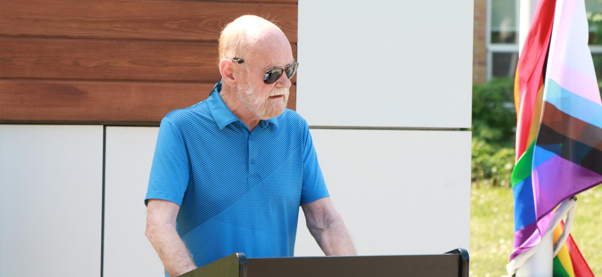 Dr. Common speaking at the podium during the Pride Flag raising ceremony