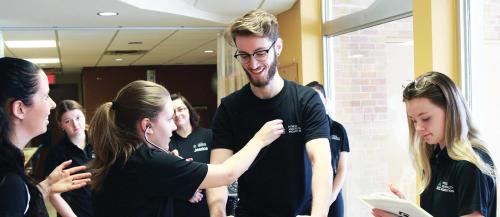 A female Fitness and Health Promotion student checks the  heart-rate of a smiling male student.