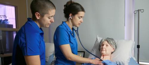 Nursing students with an elderly sim manikin checking vitals