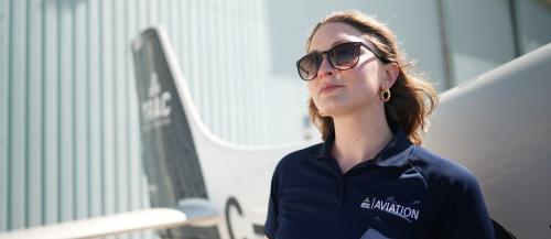 Aviation student Amanda looking up at the sky standing in front of a plane