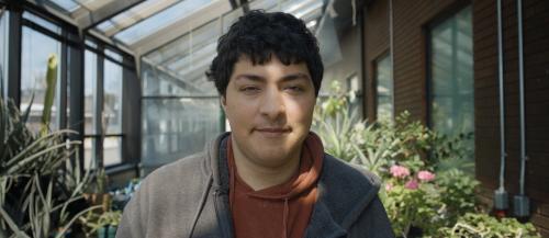 CICE student looking straight at camera with SONE greenhouse in background